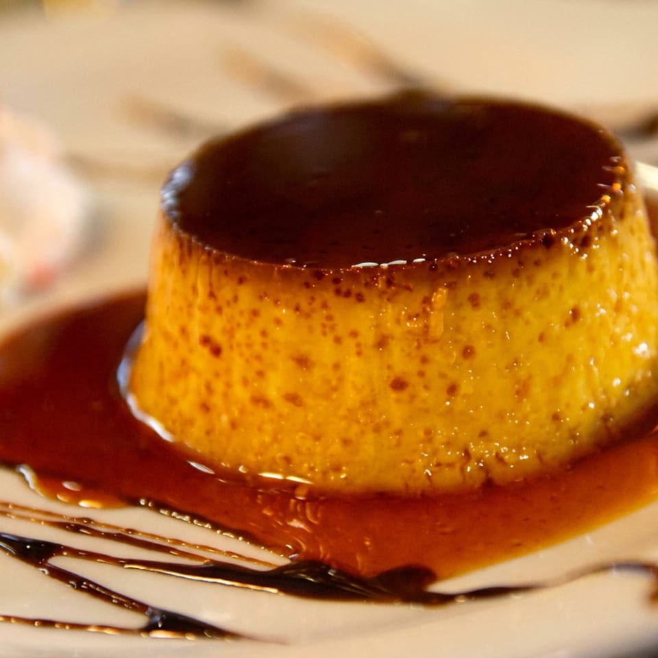 Caramel flan served on a white plate with caramel sauce and chocolate drizzle.