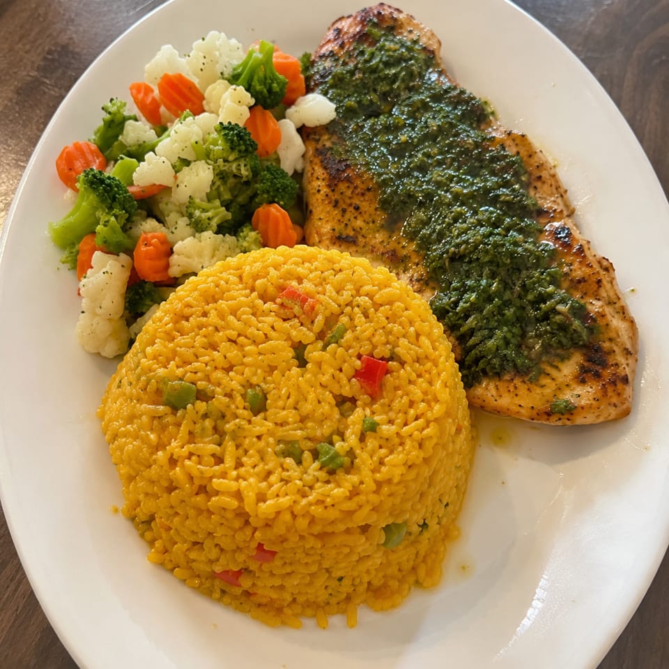 Grilled fish topped with herbs, yellow seasoned rice, and mixed steamed vegetables on a white plate.
