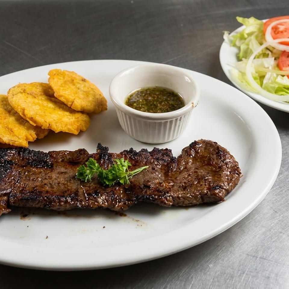 Grilled steak with golden fried plantains, dipping sauce, and a side salad of lettuce, tomato, and onion on white plates.